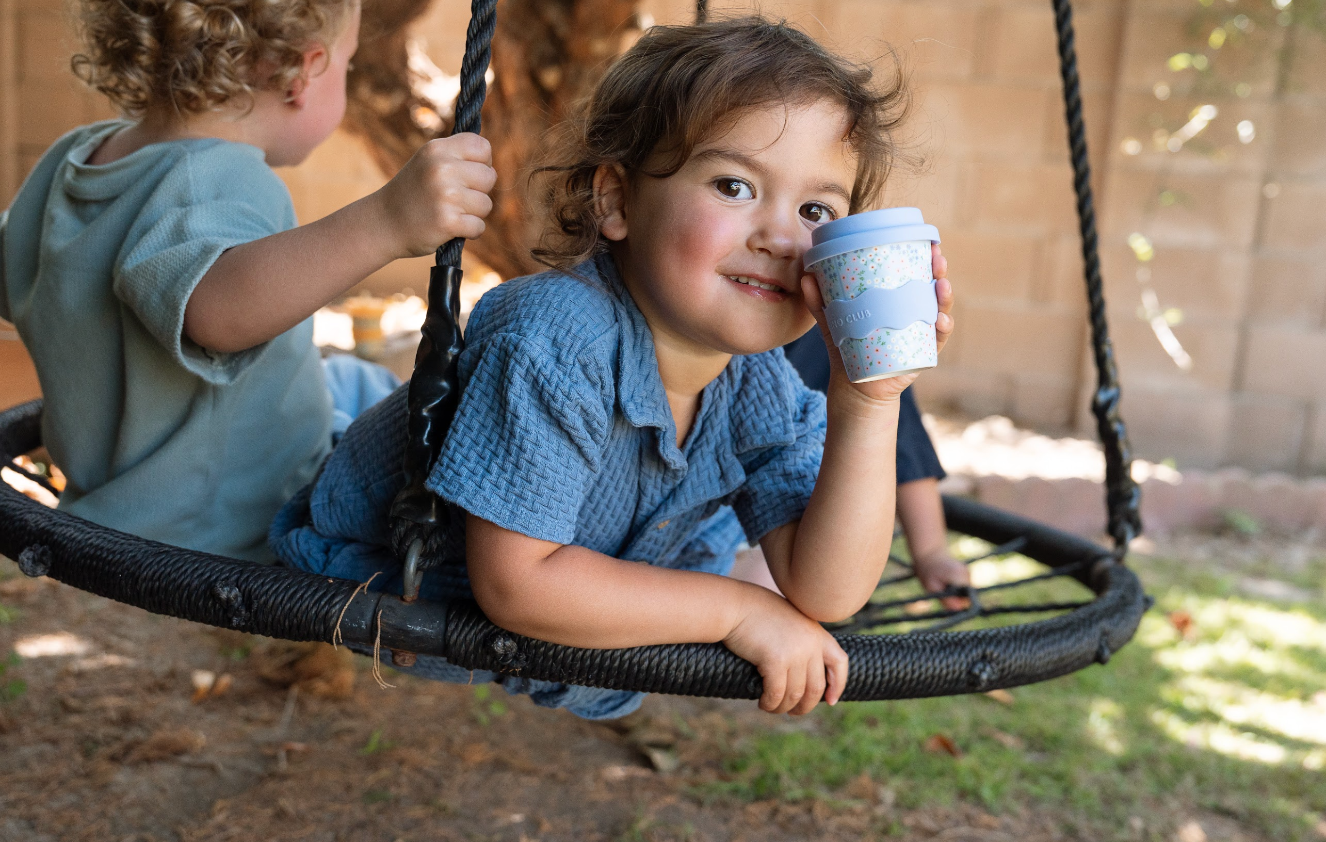 Baby holding a light blue floral babychino cup with lid and straw